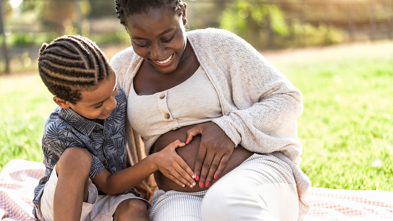 Happy black woman expecting other baby - Mother and son touching pregnant belly doing heart shape with hands jpeg
