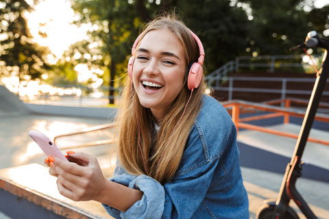 Positive young teenage girl outside in park holding mobile phone